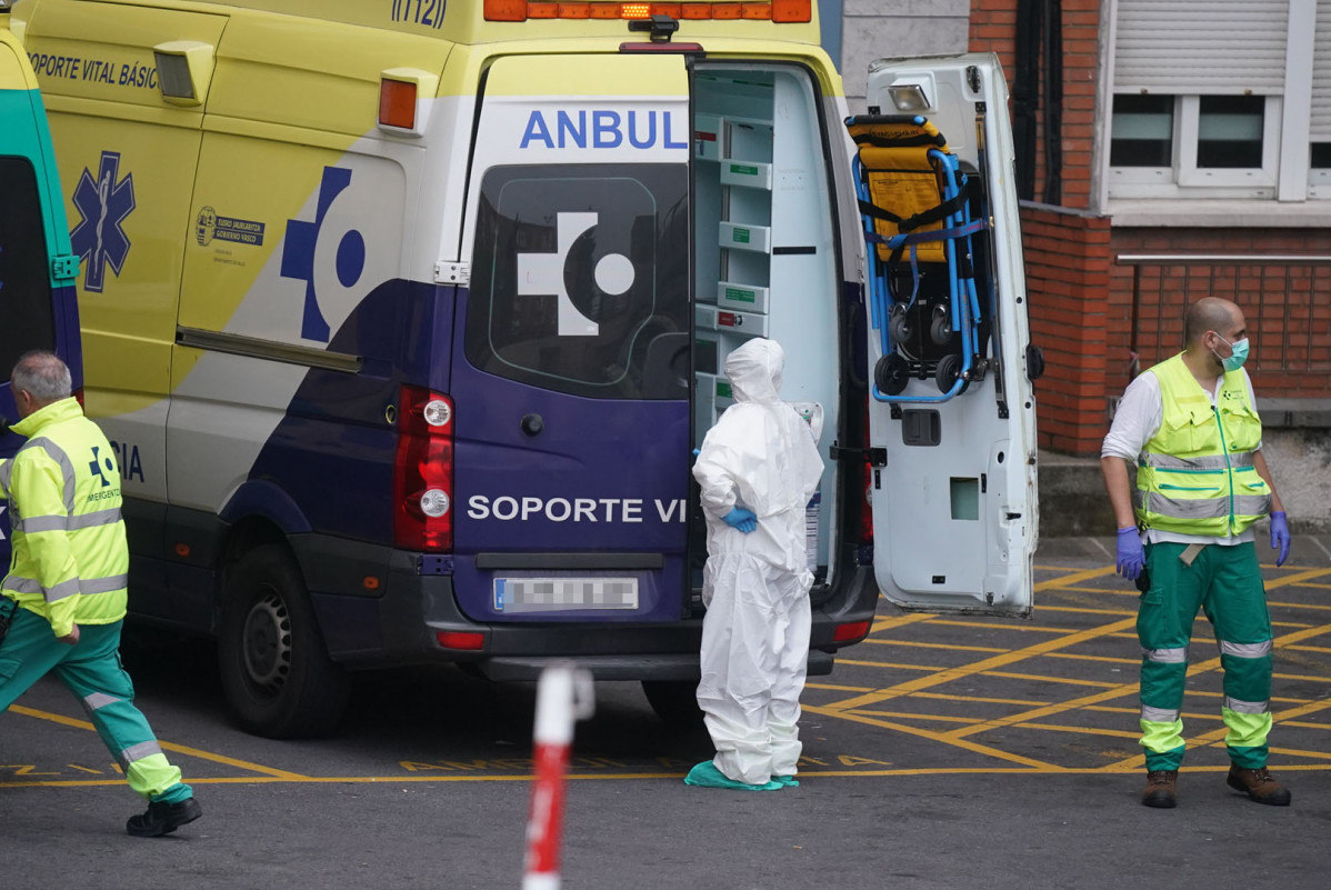 Varios sanitarios protegidos, uno con un traje y otro con mascarilla y guantes de látex, junto a una ambulancia en el Hospital Universitario Cruces, uno de los hospitales públicos vascos de referenc