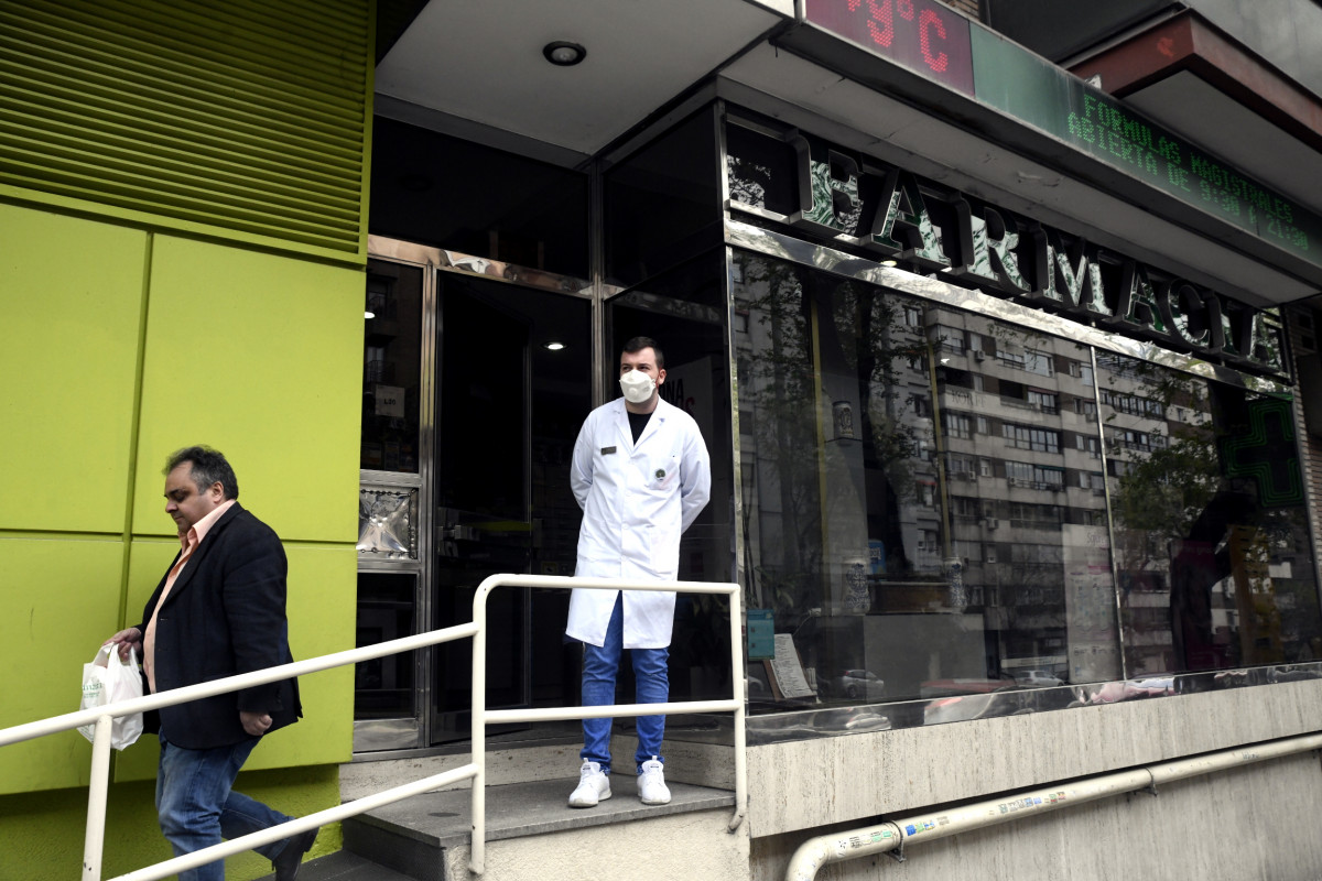 Un farmacéutico protegido con mascarilla en la puerta de una farmacia.