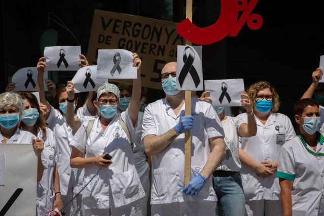 Trabajadores sanitarios protegidos con mascarilla se reúnen a las puertas del Hospital Clínic de Barcelona con pancartas y crespones negros para reivindicar contratos dignos y más personal, así como recordar a los fallecidos por la crisis del Covid-19.