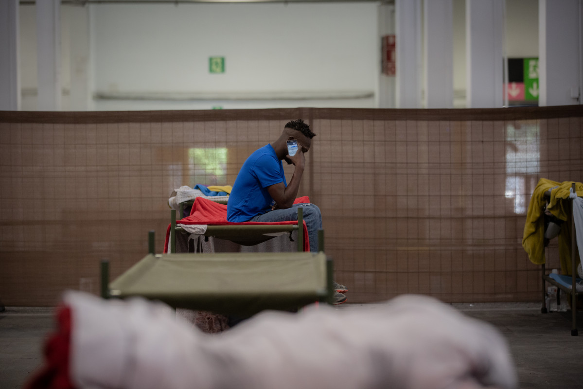 Un hombre consulta su móvil en su cama en el interior de las instalaciones del albergue de Fira Barcelona, habilitado por la crisis de la pandemia del coronavirus para 225 personas sin techo. En Barc