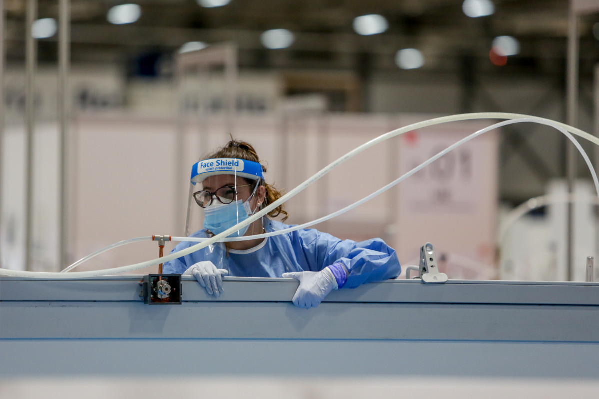 Una sanitaria protegida con mascarilla, guantes y pantalla protectora se asoma por encima de una mampara durante la lectura de pasajes de ‘El Quijote’ para los sanitarios y pacientes del Hospital temporal de IFEMA para enfermos con Covid-19 en conmemoraci