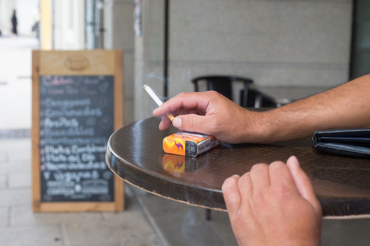 Una persona fuma en una terraza durante el primer día de la prohibición de realizarlo en la vía pública en Galicia si no existe una distancia de dos metros de separación con otras personas para e