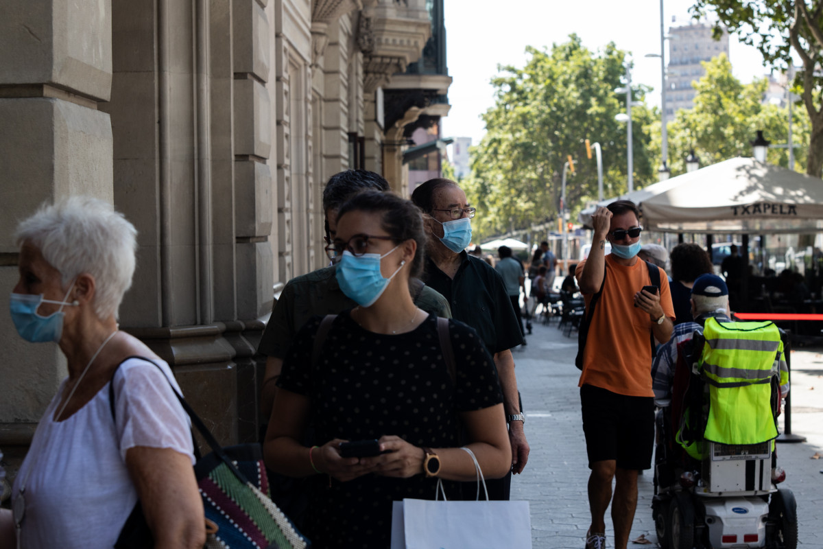 Decenas de personas protegidas con mascarilla hacen cola para entrar en una biblioteca, en Barcelona, Catalunya (España).