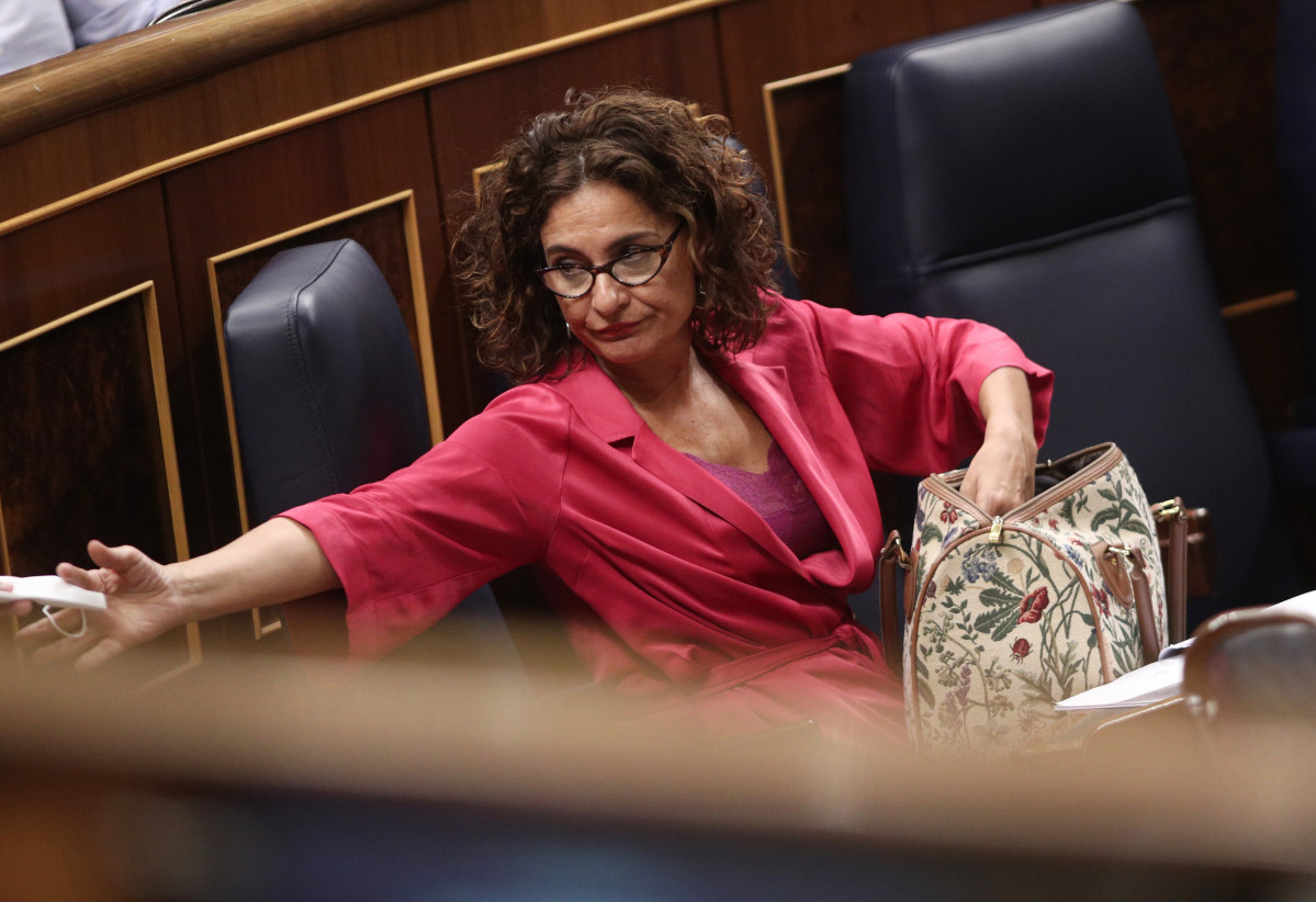 La ministra de Hacienda, María Jesús Montero, busca en su bolso una mascarilla y un diputado le presta otra  en el Congreso durante la sesión plenaria.