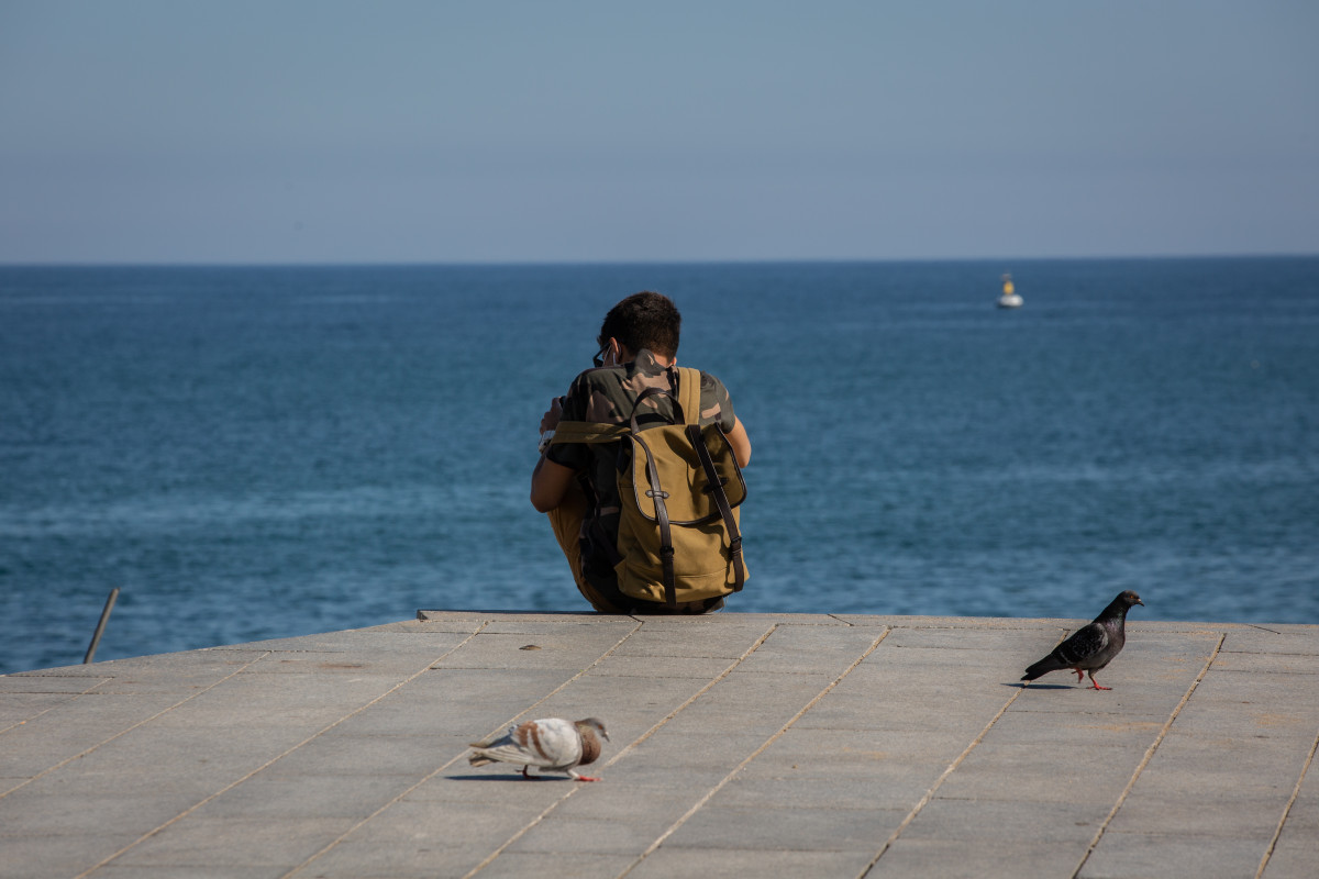 Un joven sentado en el Paseo Marítimo de la Playa de la Barceloneta.