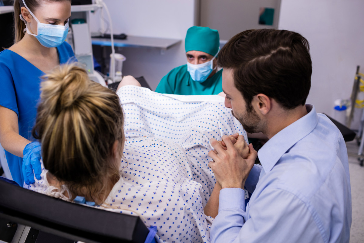 Equipo medico examina mujer embarazada parto mientras que hombre sostiene su mano