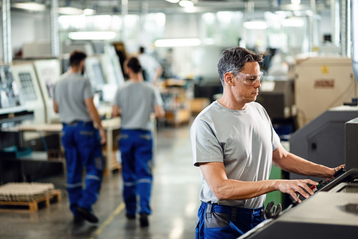 Trabajador adulto medio que opera maquina cnc mientras trabaja instalacion industrial