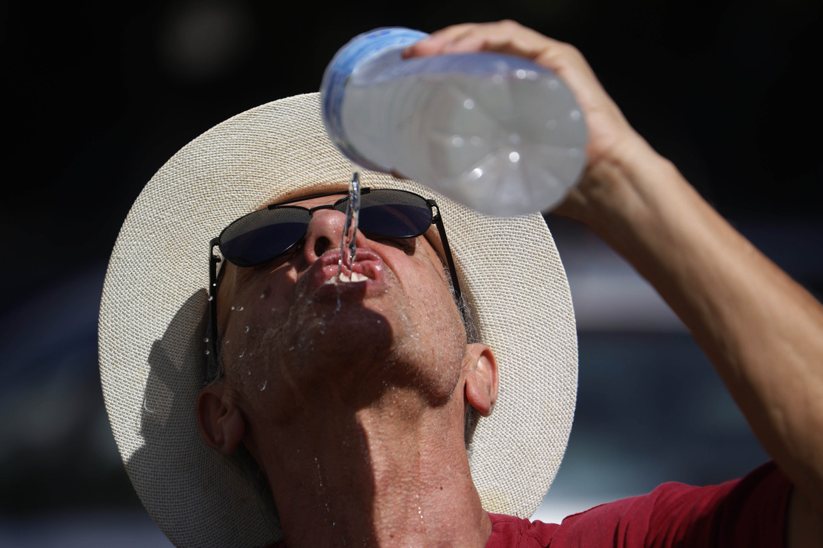 GRAFAND2887. CÓRDOBA, 09/08/2024.- Un hombre se refresca con agua de una botella mientras camina por el Puente Romano de Córdoba, este viernes en el que arranca una nueva ola de calor que podría se