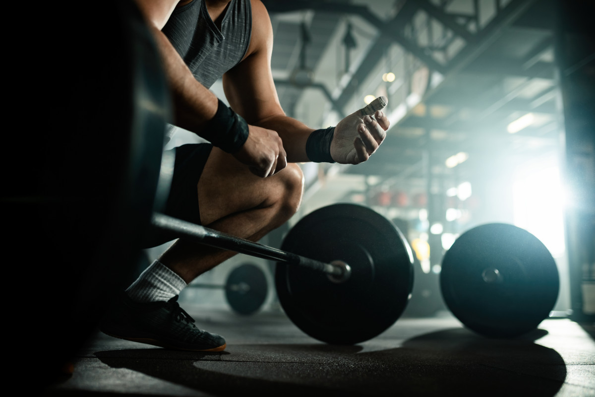 Low angle view unrecognizable muscular build man preparing lifting barbell health club