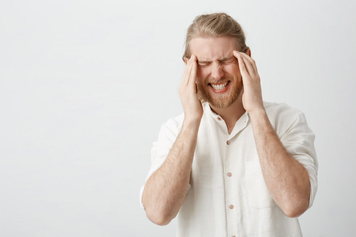 Indoor portrait caucasian blond man with beard suffering from migraine headache holding fingers temples